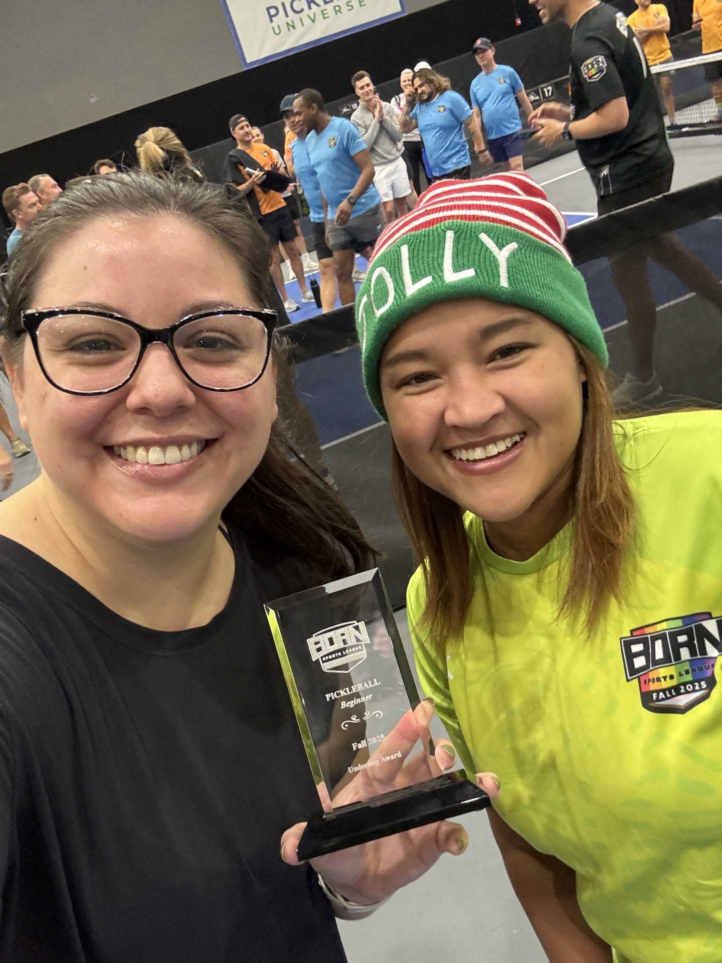 Two people smiling and holding an Underdog award trophy at a pickleball event